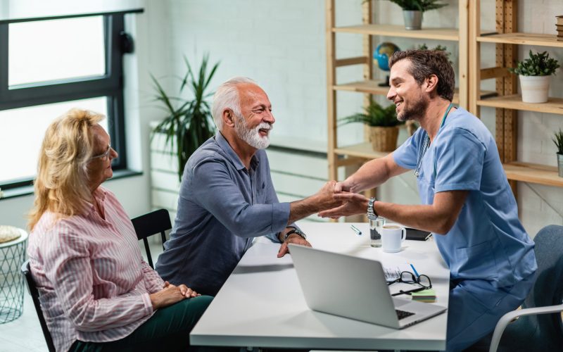 Happy male doctor shaking hands with senior man who came to medical appointment with his wife.